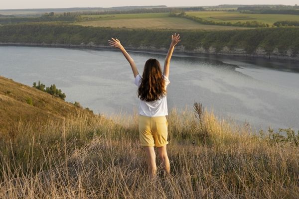 Girl with raised arms looks down to a river